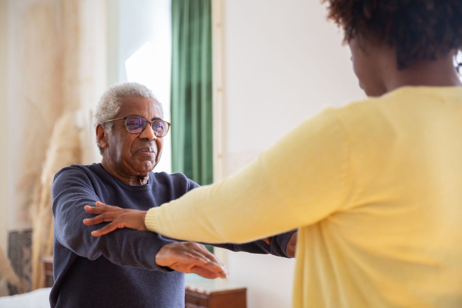 Therapist guiding an older adult through a mobility exercise at home